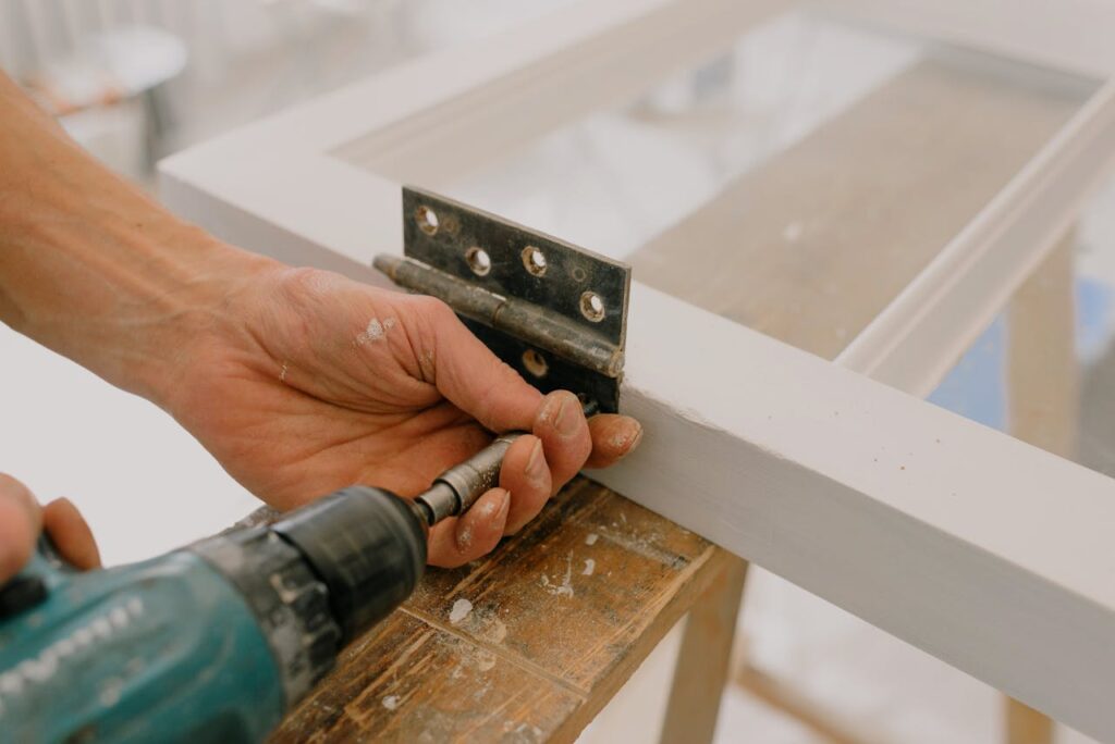 pexels-photo-5691518 Crop unrecognizable worker drilling metal hinge on white window frame during house renovation