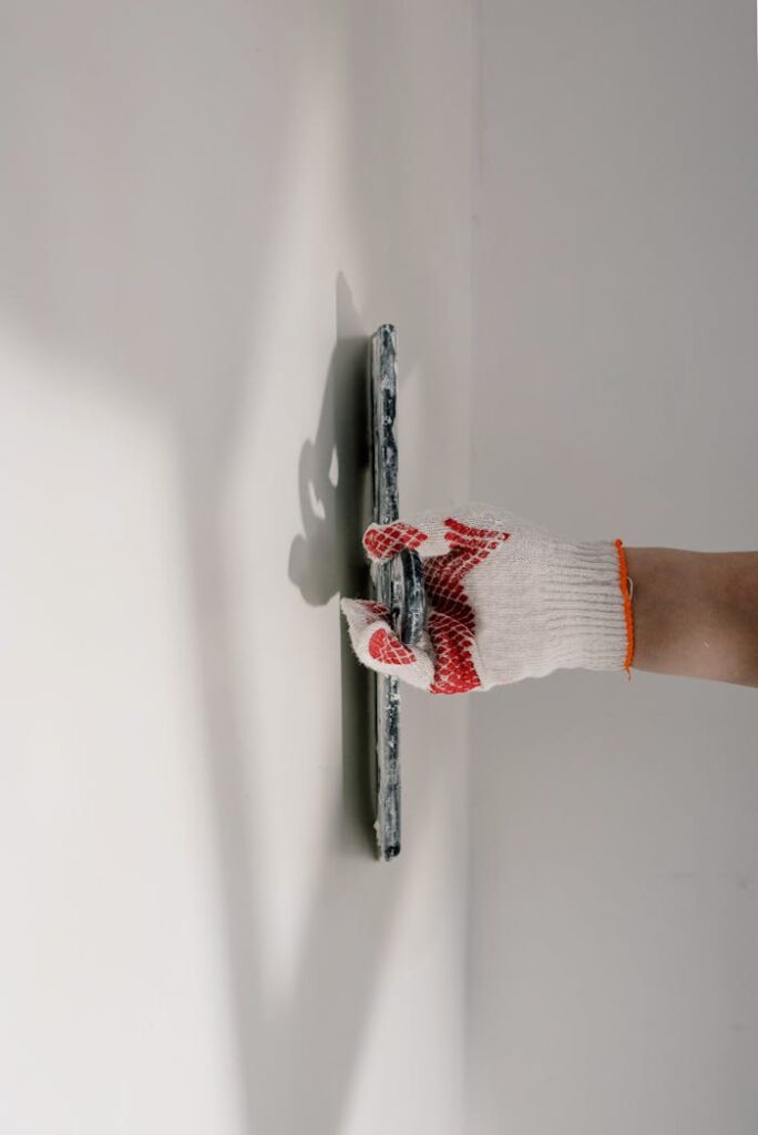 Crop anonymous painter in gloves preparing wall for painting works during renovation process in apartment